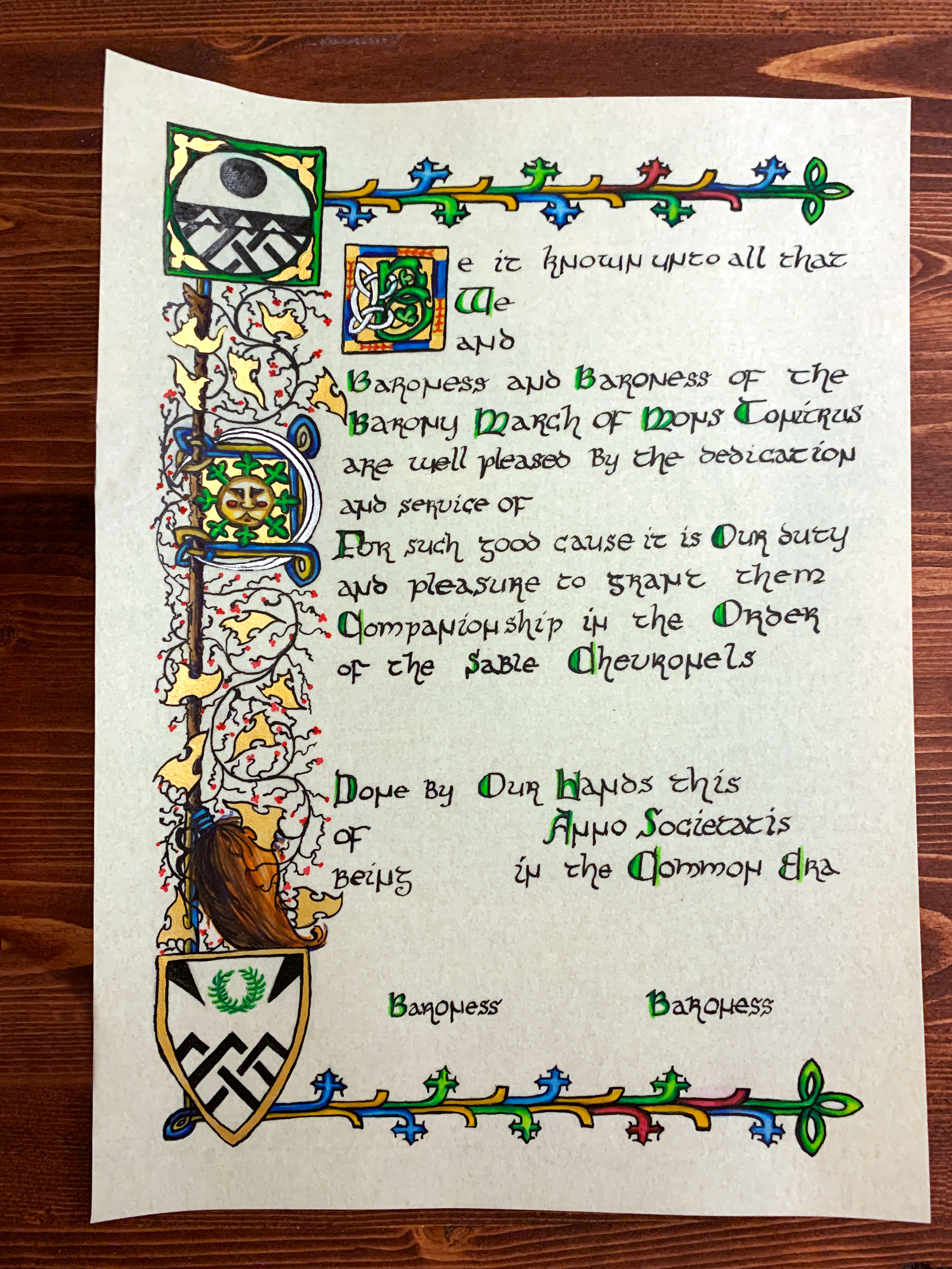 A medieval scroll award in progress: the coloring stage, inks have been added back onto the colored work, darkening the form and outlines of artwork. The final stage is to add white-work (highlights).